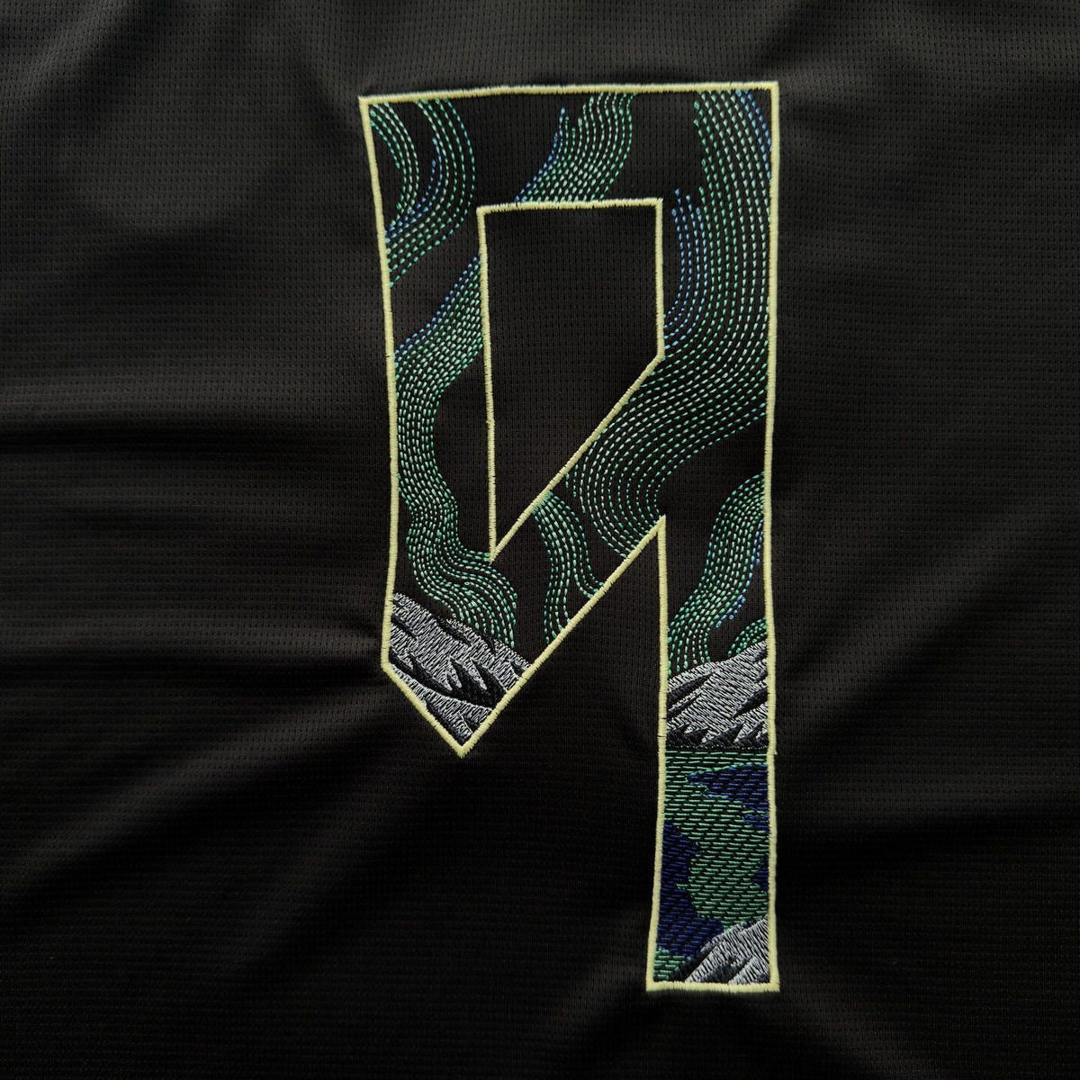 Haaland 9 embroidered with green and blue Northern Lights over grey mountains, outlined in pale yellow