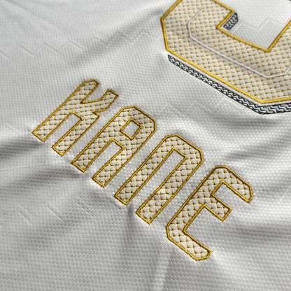 Close-up of the gold-outlined KANE nameset with geometric fill stitching on the white away jersey
