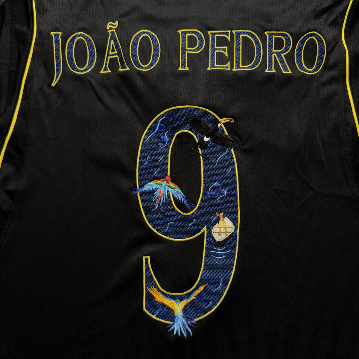 The embroidered 9 with macaws, a toucan and an Amazon river boat on deep navy