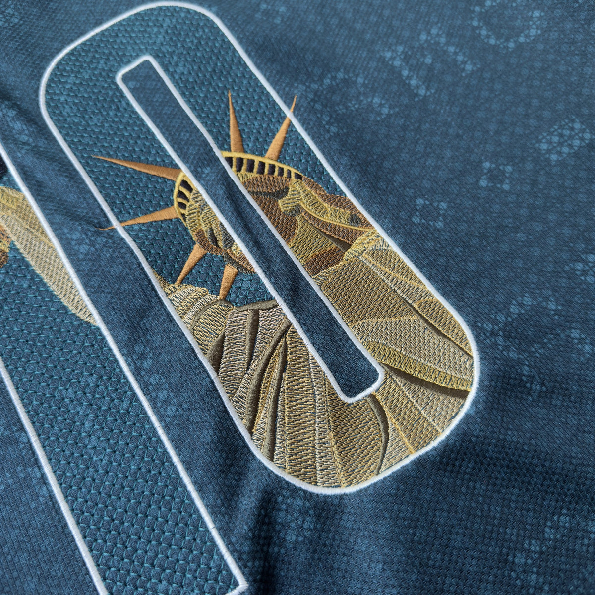 Close-up of the Statue of Liberty's gold-rayed crown breaking out of the 0, outlined in cream