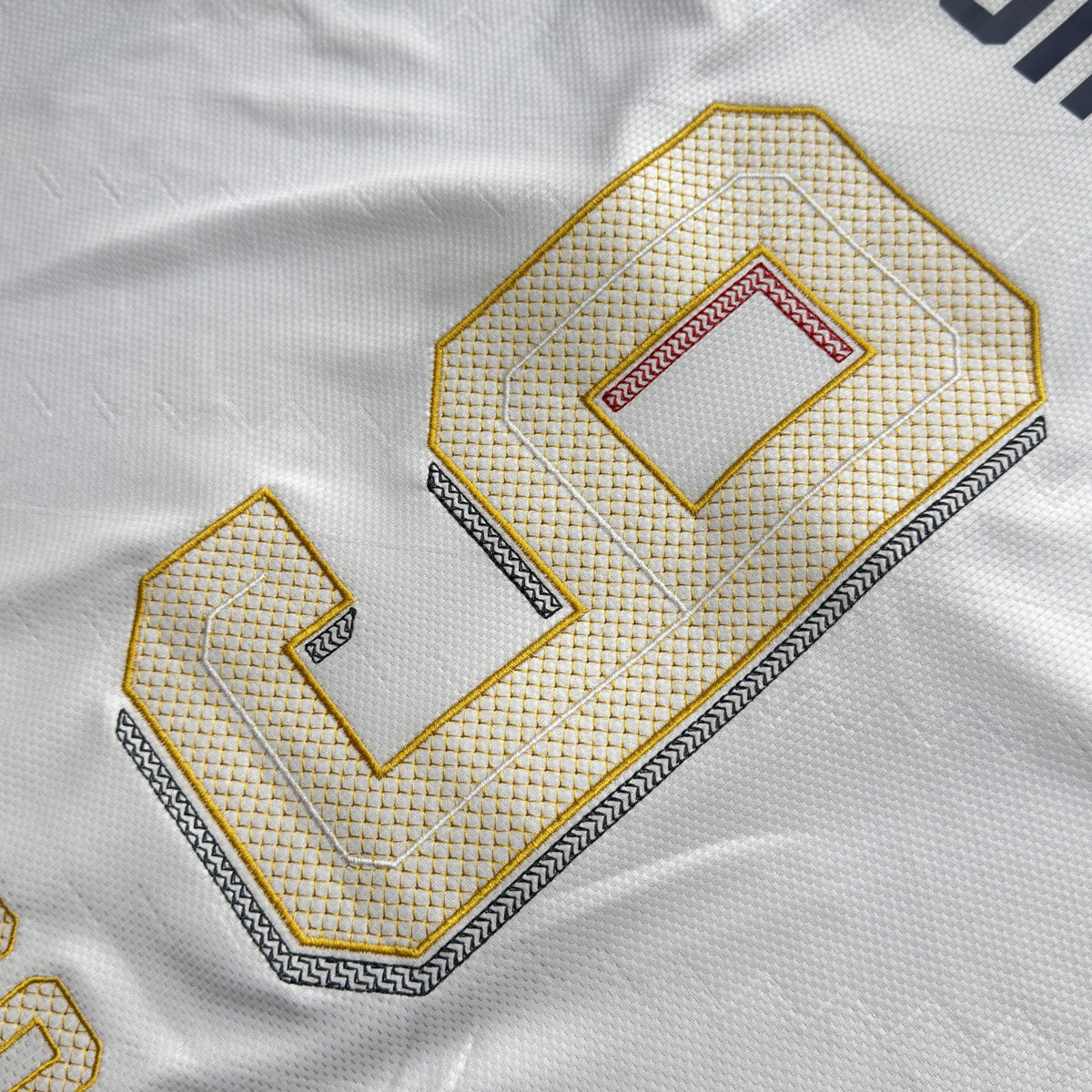 Close-up of Kane's 9 embroidered in white and gold with geometric fill stitching