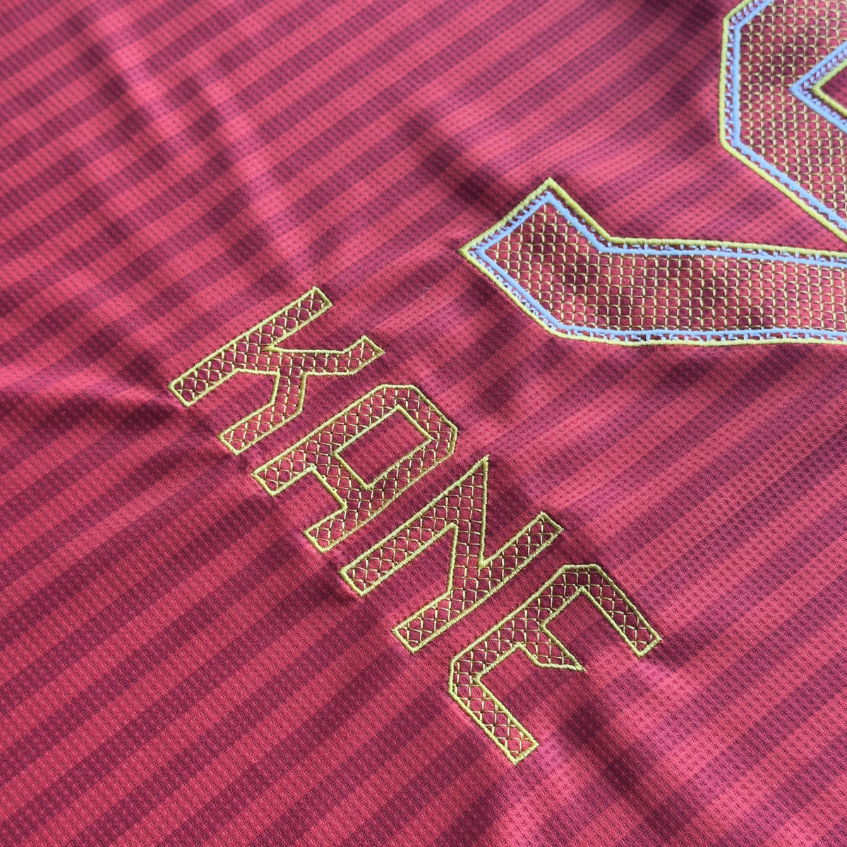 Close-up of the gold-outlined KANE nameset and 9 embroidery on the red Bayern home jersey