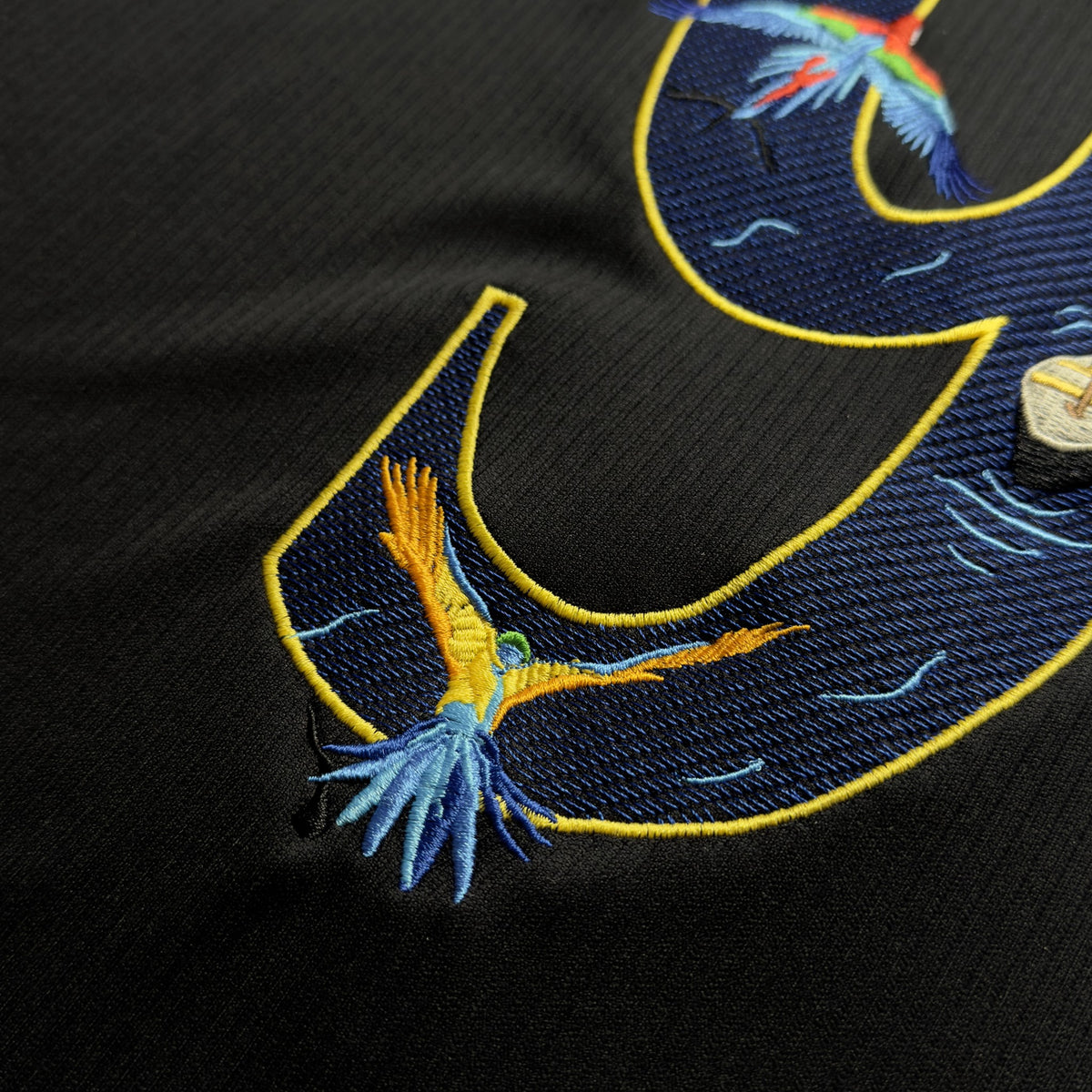 Close-up of embroidered macaws in flight across the top of the 9