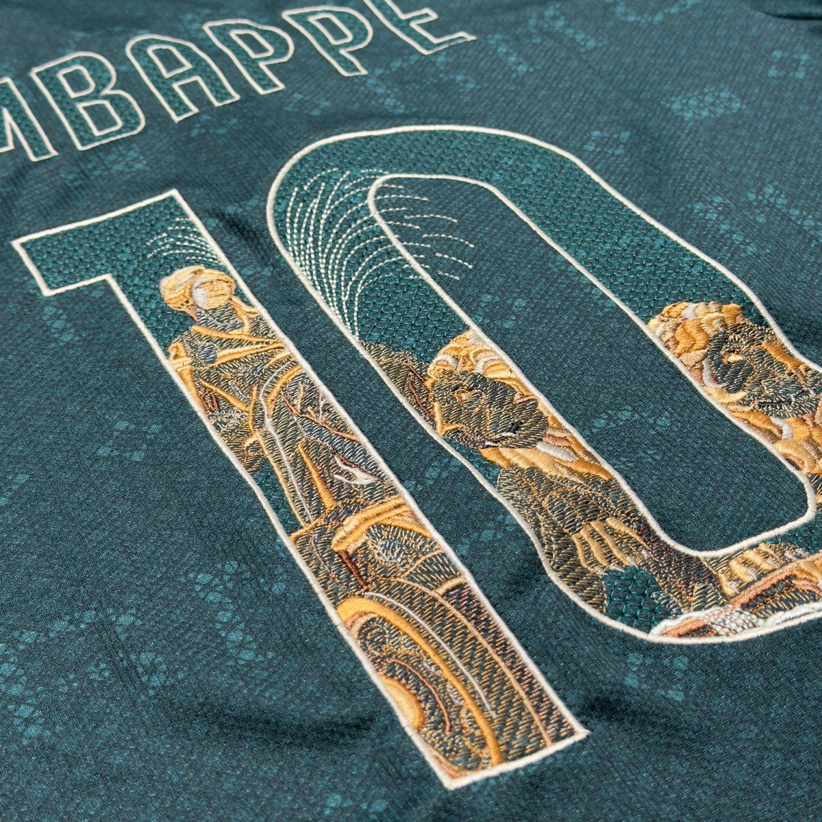 Angled view of the Mbappé 10 on the green away jersey, with the Cibeles statue, lions and fountain spray embroidered in gold and stone tones