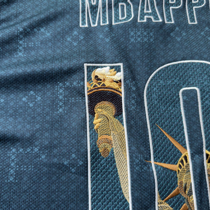 Detail of the Statue of Liberty's torch rising inside the 1, below the MBAPPÉ name