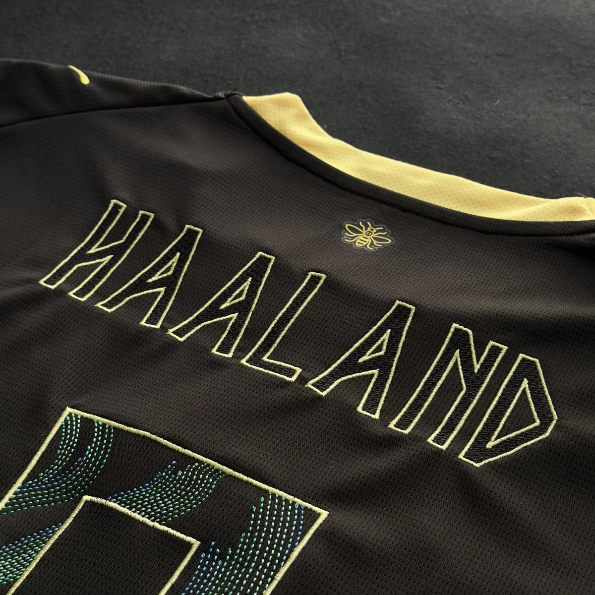 HAALAND name embroidered in pale yellow outline below the bee on the back neck
