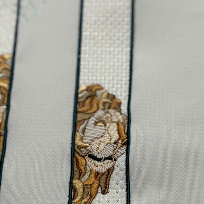 Macro detail of an embroidered Cibeles lion in warm stone and gold tones inside the number 1