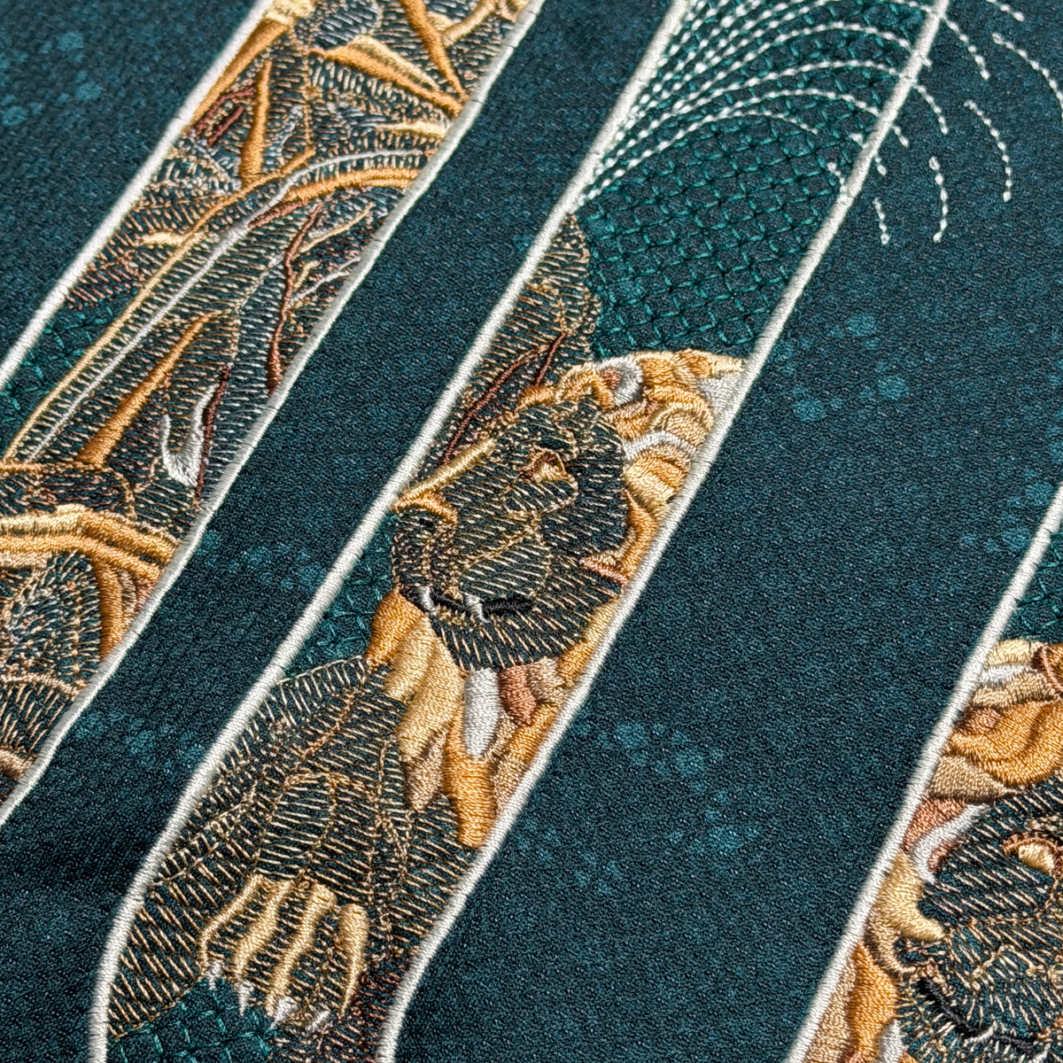Macro detail of a Cibeles lion embroidered in gold and stone tones inside the number 0, with the fountain spray above