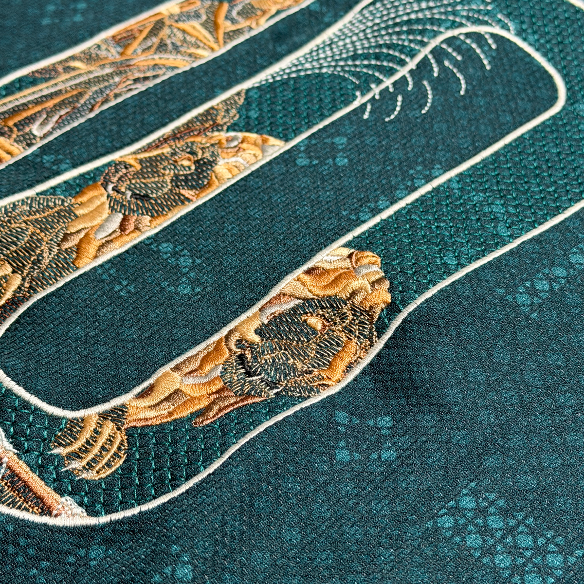 Close-up of the lions embroidered in gold and stone tones curving through the 0, with open geometric stitching on the green away jersey