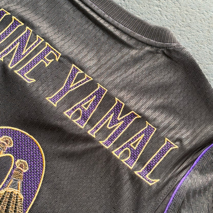 Detail of YAMAL in gold-outlined modernista lettering, stitched over the jersey's textured knit