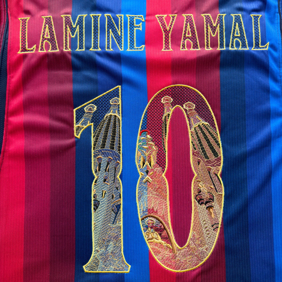Close-up of the embroidered back: LAMINE YAMAL in gold modernista lettering above the Sagrada Família 10, stitched straight onto the stripes