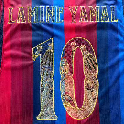 Close-up of the embroidered back: LAMINE YAMAL in gold modernista lettering above the Sagrada Família 10, stitched straight onto the stripes